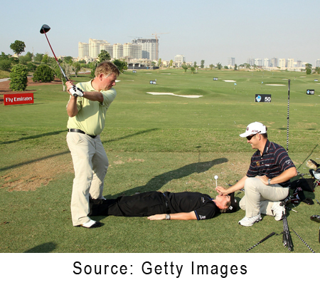 Louis Oosthuizen holds a tee over the face of Rory McIlroy as trick shot expert David Edwards hits a full drive during the Dubai World Championship.
